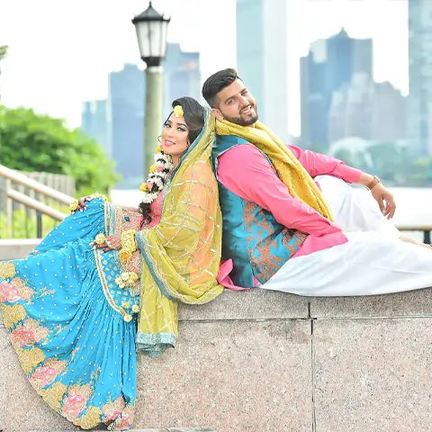 Rezuena Ahmed, New York, in a turquoise and yellow outfit posing back to back with a man in a pink kurta