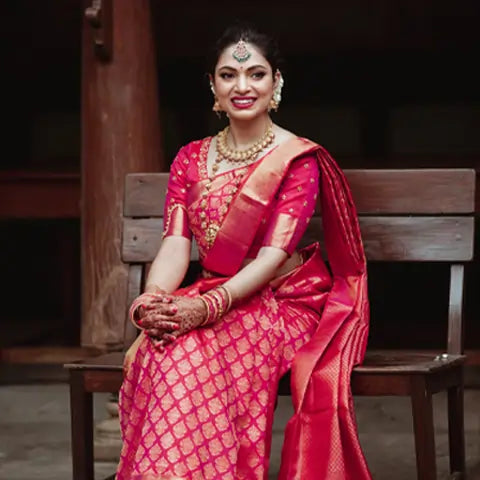 Anusha Venugopal, San Francisco, seated on a wooden bench in a pink and gold silk saree