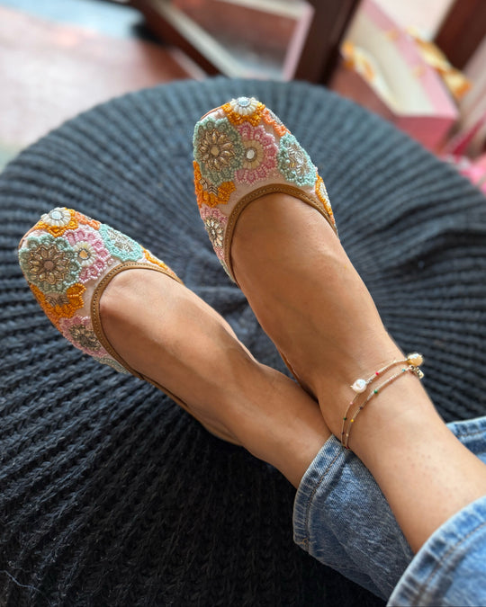 Colorful embroidered flats worn by a person sitting on a dark cushion.